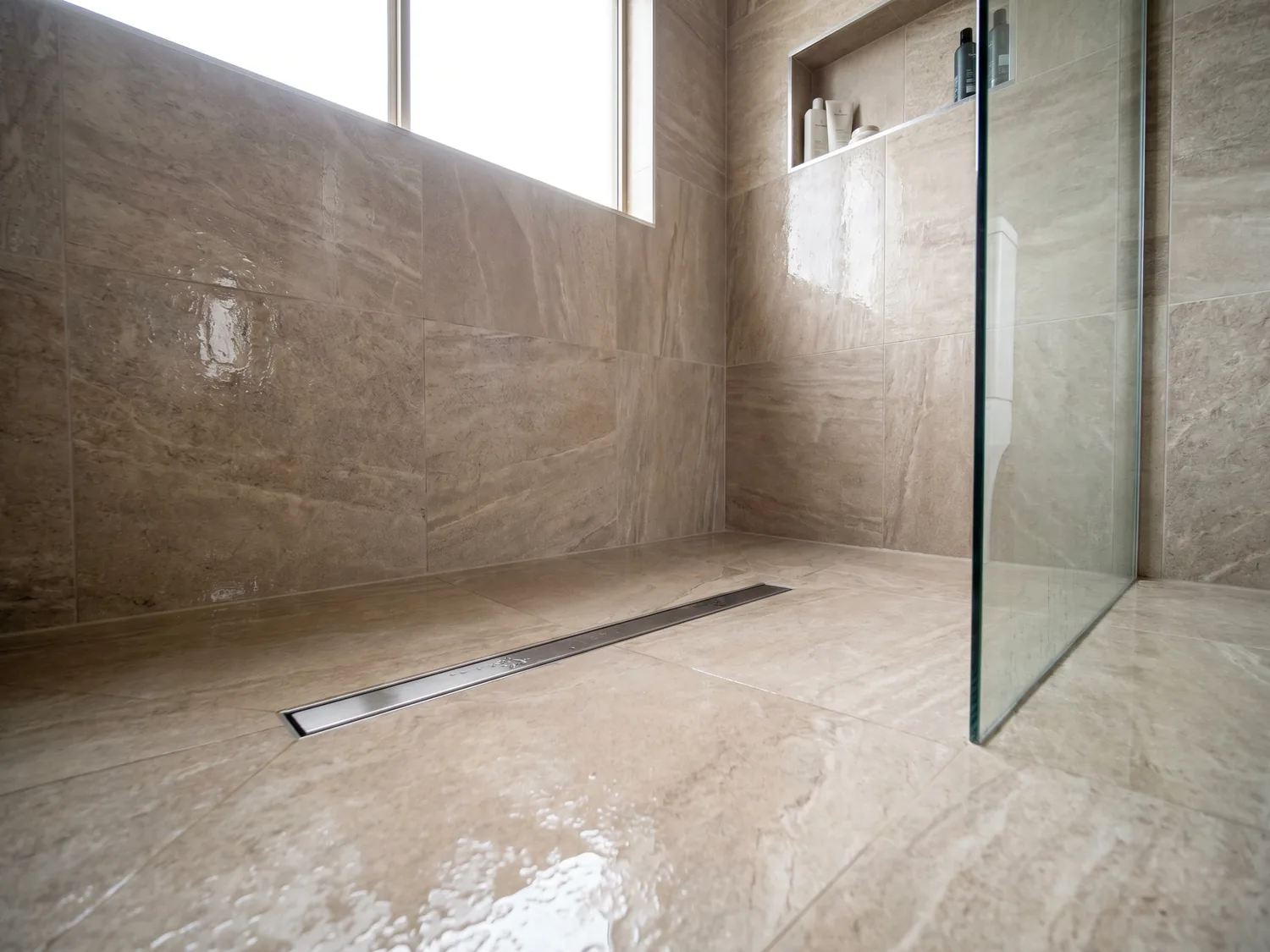 Walk-in tiled shower with linear drain and glass panel